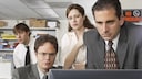 The characters Dwight Schrute (Rainn Wilson), Michael Scott (Steve Carell), Pam Beesly (Jenna Fischer), and Jim Halpert (John Krasinski) are all intently focused on a computer screen.