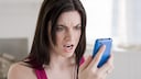 Woman looks angrily at a smartphone.