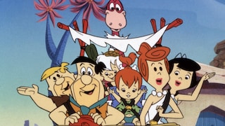 Animated scene from "The Flintstones": Several characters are sitting together in an open Stone Age vehicle. Two characters are visible in the front, one at the wheel and the other in the passenger seat, with more characters and a small child behind them. A pink dinosaur with a long neck towers over the vehicle. The car has a roof made of wooden poles and white fabric. In the background, stylized trees with violet-blue trunks and pink leaves stand against a light blue sky.