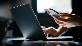 iPhone in hand, next to a laptop