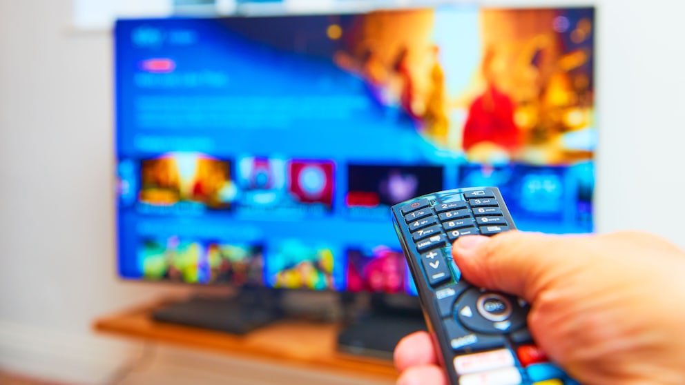 TV remote in the foreground, blurred television in the background