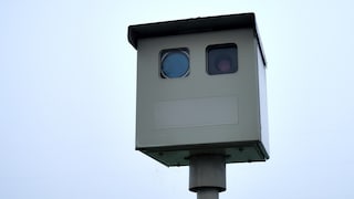A speed camera is positioned by the roadside.