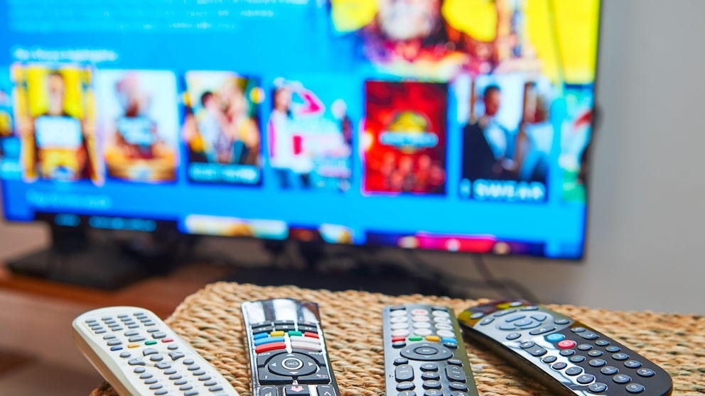 Several remote controls are lying on a table in front of a television.
