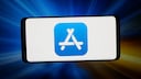 A smartphone in landscape orientation with a large app store icon on a white screen. The background features blue and orange light beams with motion blur. The device is centered in the image and set against a dark background.