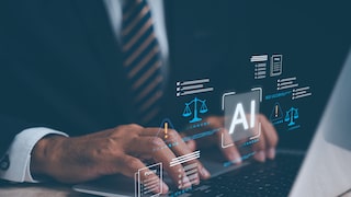 A man in a suit sits at a desk, working with AI on his laptop.