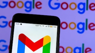 A smartphone is held against a blurred background featuring multiple Google logos. The display shows the multicolored Gmail logo on a white background. At the top of the screen, status symbols, the time "9:25," the "4G LTE" indicator, and a battery level of "100" are visible. The smartphone is slightly tilted and occupies a large portion of the image. In the background, the colorful Google logos in blue, red, yellow, and green repeat.