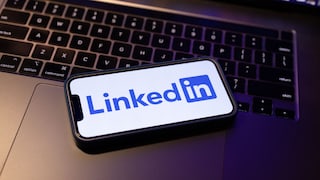 An iPhone displaying the LinkedIn logo rests on a MacBook keyboard.