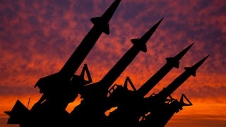 Silhouette of weapon-capable missiles against a sunset-drenched red sky
