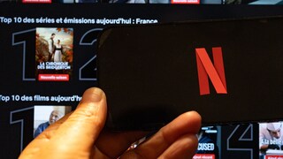 Netflix logo on a smartphone, with streaming tiles in the background on Netflix