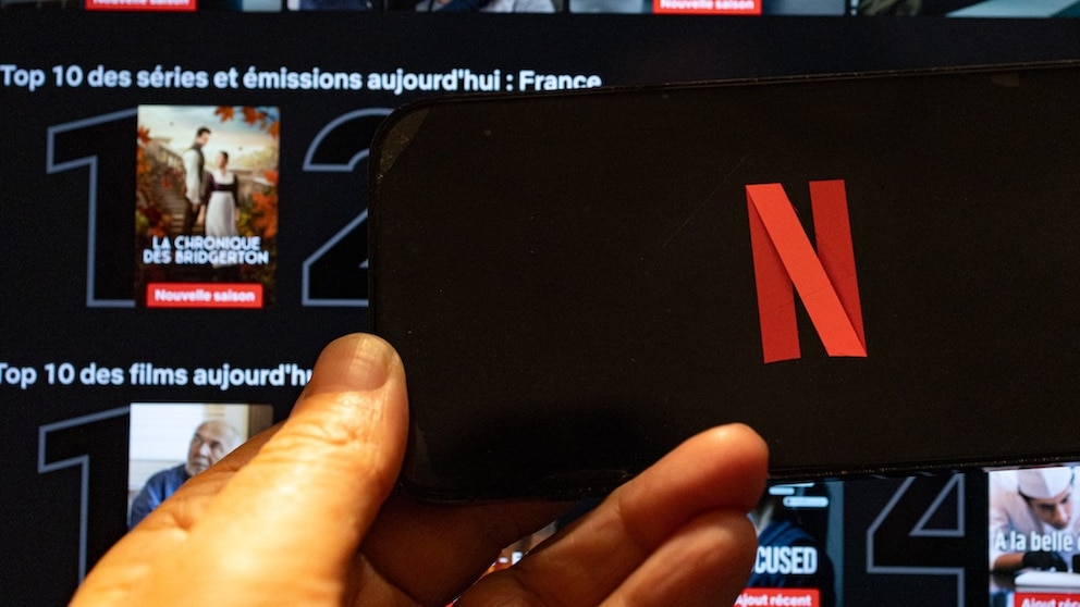 Netflix logo on a smartphone, with streaming tiles in the background on Netflix