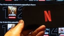 Netflix logo on a smartphone, with streaming tiles in the background on Netflix