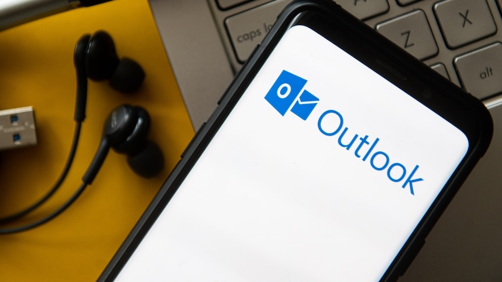 Outlook logo on a smartphone, along with a keyboard and headphones