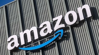 A skewed view of a large Amazon logo with a blue arrow on a facade made of vertical metal panels against a blue sky.