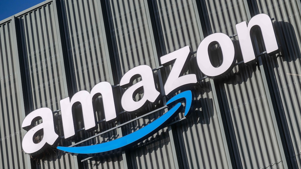 A skewed view of a large Amazon logo with a blue arrow on a facade made of vertical metal panels against a blue sky.