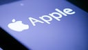 Close-up of a smartphone display featuring a white Apple logo and the Apple name on a blue background.