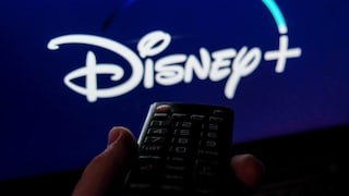 A remote control is held in front of a television. The Disney+ logo is visible, though blurred, on a blue background on the screen.