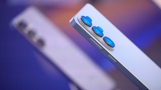 Close-up of the back of a light-colored Samsung smartphone with three camera lenses, with a blurred second device from the same series in the background.