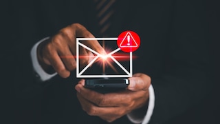 A person holds a smartphone and taps on a displayed envelope icon. Next to it, there's a red warning symbol with an exclamation mark. The image illustrates a suspicious or potentially dangerous email.