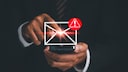 A person holds a smartphone and taps on a displayed envelope icon. Next to it, there's a red warning symbol with an exclamation mark. The image illustrates a suspicious or potentially dangerous email.