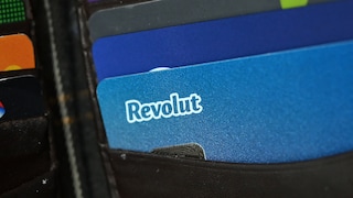 Several bank and payment cards are tucked into a black cardholder. In the foreground, a blue Revolut card with a white Revolut logo is visible. Behind it, more cards in various colors are protruding.