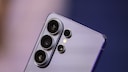 Close-up of the back of a silver Samsung smartphone with multiple camera lenses against a blurred blue-violet background