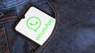 A smartphone with the WhatsApp logo open is tucked into the pocket of blue jeans.