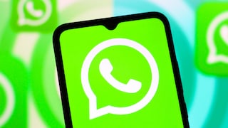 A smartphone prominently displaying the WhatsApp logo is in the foreground. On the screen, the white WhatsApp symbol is visible against a green background. In the blurred background, additional enlarged WhatsApp logos in green and white appear.