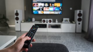 Only a person's hand holding a remote control is visible. It seems the TV on the living room wall was just turned on.