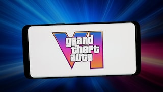 A smartphone is positioned horizontally against a blue and pink glowing background. On the white display, the logo for "Grand Theft Auto VI" is visible. Behind the text, a large Roman numeral six features a gradient transitioning from blue to pink to orange.