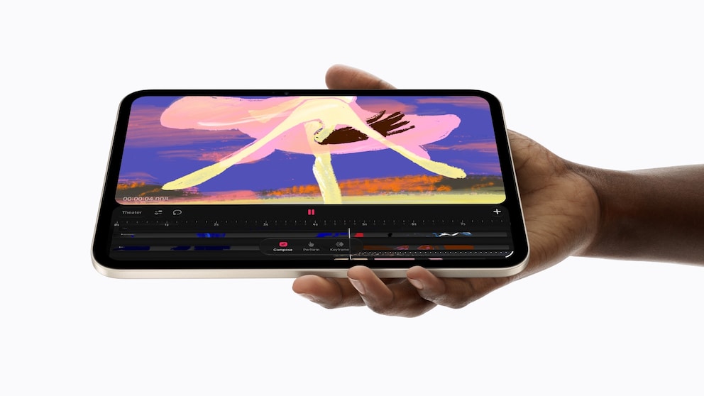 A hand holds an iPad mini in landscape orientation against a white background. The display shows animation software with a timeline and several editing tools open. Above it is a colorful drawing featuring pink, yellow, and violet brushstrokes. The tablet has a black display frame and a light metal casing.