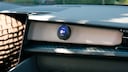 A round OOONO device is mounted on the passenger side of a dashboard. The display shows a speed camera warning with a speed limit sign of 80 km/h and a distance indication of 400 meters. To the left, part of the infotainment screen is visible.