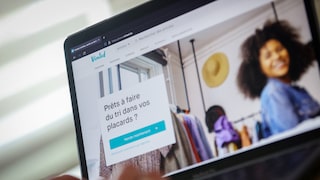A laptop displaying the Vinted website. On the French-language homepage, the Vinted logo, a wardrobe filled with clothes, and a person in the background are visible. In the foreground, there's a field with the text "Prêts à faire du tri dans vos placards?" and a turquoise button.