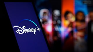 A smartphone displaying a glowing Disney Plus logo against a blurred, colorful background featuring people and screens.