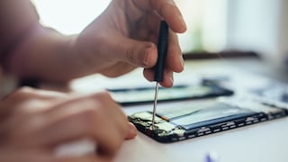 Hands repair the opened interior of a smartphone with a screwdriver on a table.