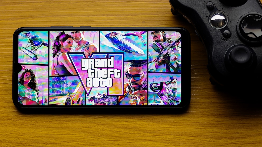 A smartphone featuring a colorful "Grand Theft Auto VI" graphic sits next to a black controller on a wooden table.