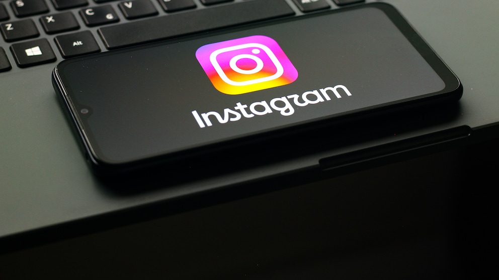 The Instagram logo is visible on a smartphone, which is resting on a laptop keyboard.