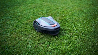 A gray robotic lawn mower with turquoise details moves across a lush green lawn.