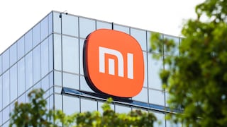 Xiaomi logo on the glass facade of a modern building, partially framed by green trees