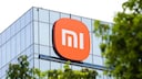 Xiaomi logo on the glass facade of a modern building, partially framed by green trees