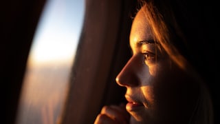 Young woman looks out of the airplane window: There are numerous myths about what you should consider when booking a flight - a new analysis has now disproved some of them