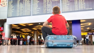 Boy Sits on Suitcase at Airport and Waits